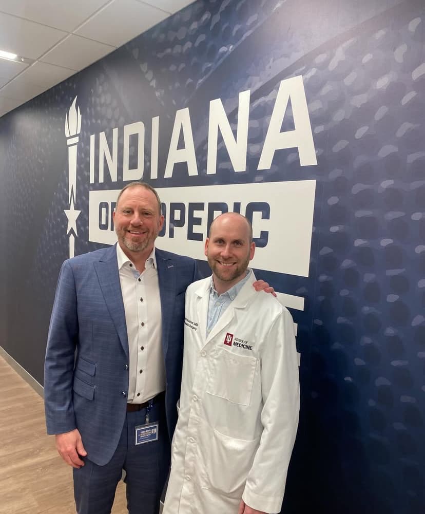 Dr. R. Michael Meneghini with an Indiana University School of Medicine fellow in front of the Indiana Orthopedic Institute wall