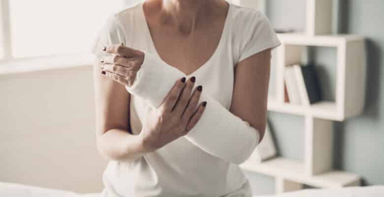 Close-up of Female Broken Arm in Plaster Cast. Caucasian Injured Woman in White T-Shirt Sitting and Holding Wrist in Gypsum Bandage with Physical Pain in Fractured Bone. Health Care concept