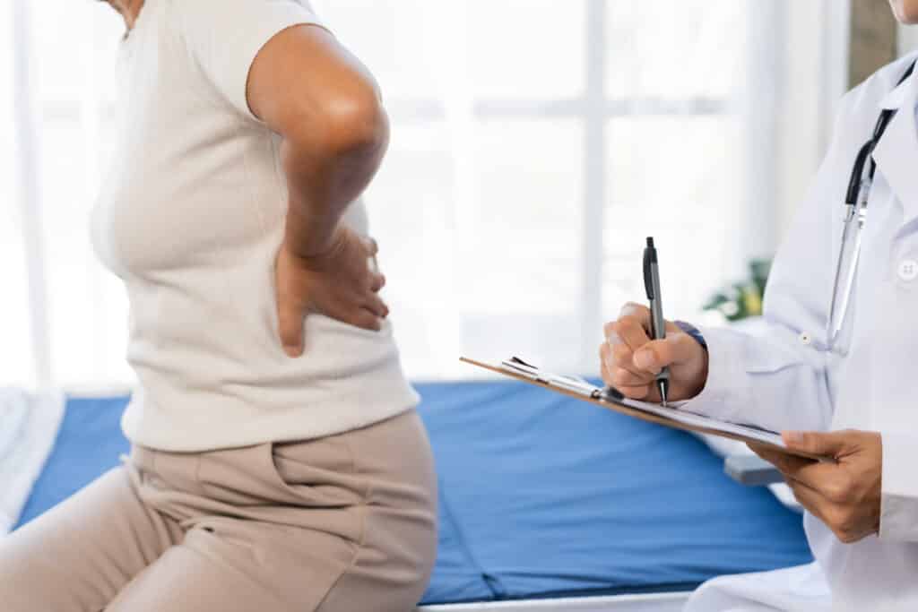 Senior woman suffering from back pain, seeking medical consultation from doctor. Doctor writing notes on clipboard during examination
