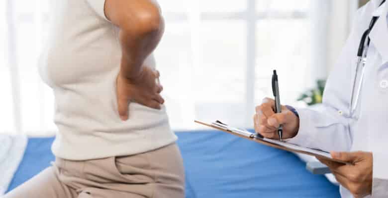 Senior woman suffering from back pain, seeking medical consultation from doctor. Doctor writing notes on clipboard during examination